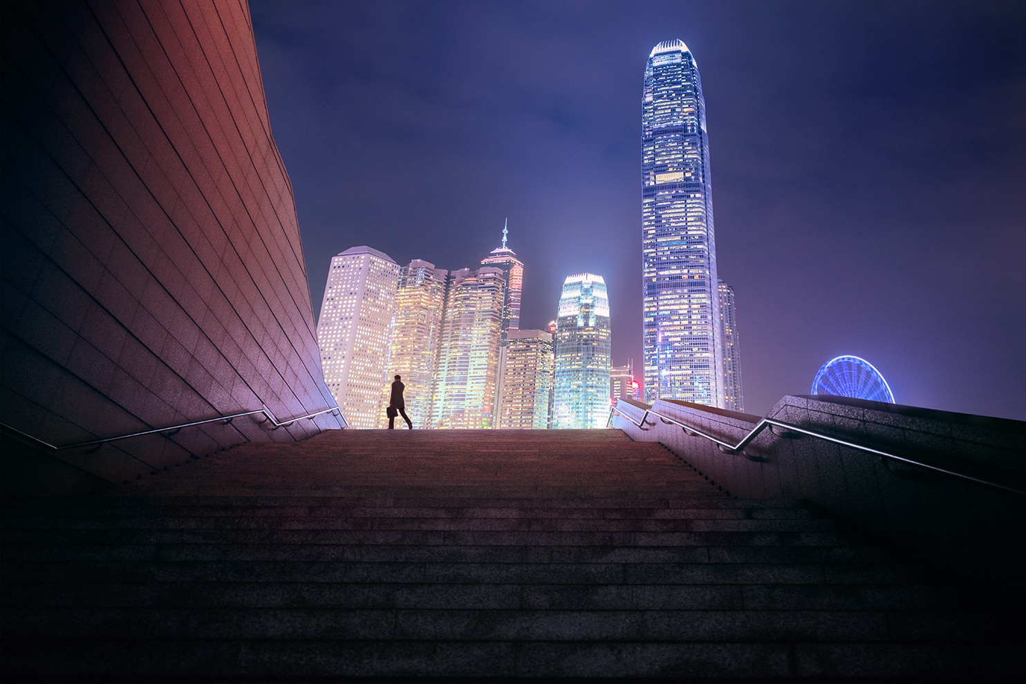 A nighttime cityscape featuring a silhouetted figure walking up a staircase towards the illuminated skyline of Hong Kong. The towering skyscrapers glow with lights, including the International Finance Centre, while a Ferris wheel is visible in the background. The composition, framed by modern architecture, creates a sense of ambition, progress, and urban energy.