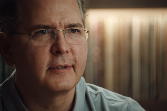 Craig Kallman, wearing a light-coloured shirt, looks focused while speaking, with a background of blurred books or records.