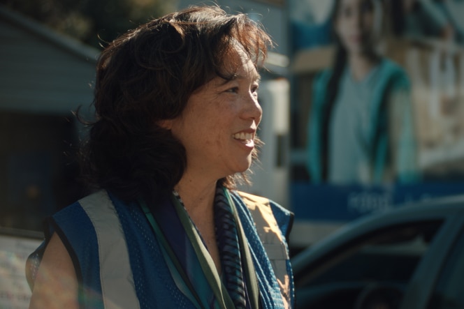 Kathy Kwan wears a reflective safety vest and a scarf and smiles while standing outdoors. 