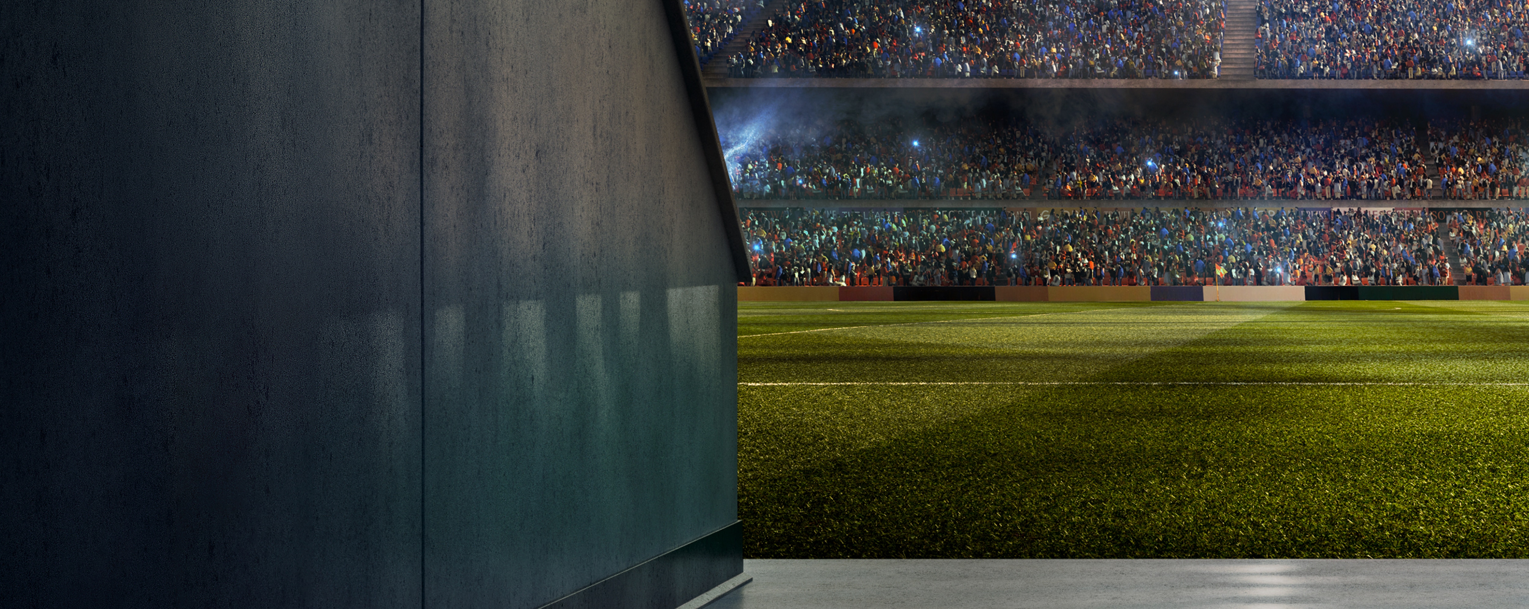 A view from the tunnel leading onto a football field in a packed stadium. The perspective shows part of the dark stadium structure on the left, contrasting with the vibrant green field and the energetic crowd in the stands, many of whom are holding up lights.